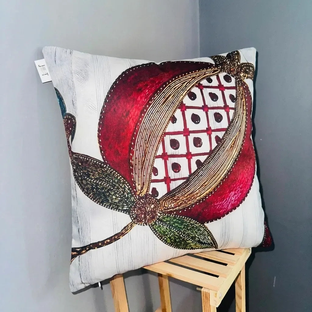 Decorative pillow with a red and gold floral design on a wooden stool against a gray wall.