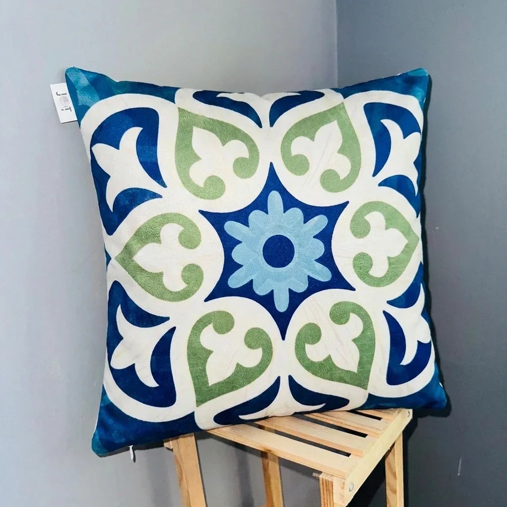 Decorative pillow with blue, green, and white pattern on a wooden stool against a gray wall.