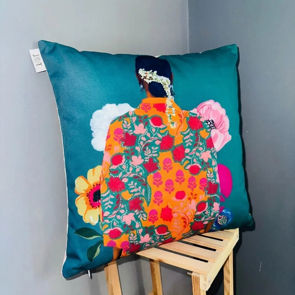 Decorative pillow with colorful floral design on a teal background, placed on a wooden stool against a gray wall.