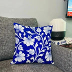 Blue floral pillow on a gray couch with a lamp and television in the background.