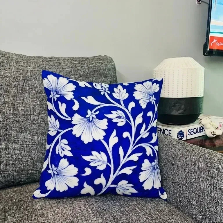 Blue floral pillow on a gray couch with a lamp and television in the background.